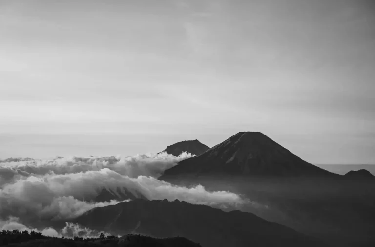 Conviction voie de l'excellence Deux volcans majestueux se dressent au-dessus des nuages dans un paysage en noir et blanc.